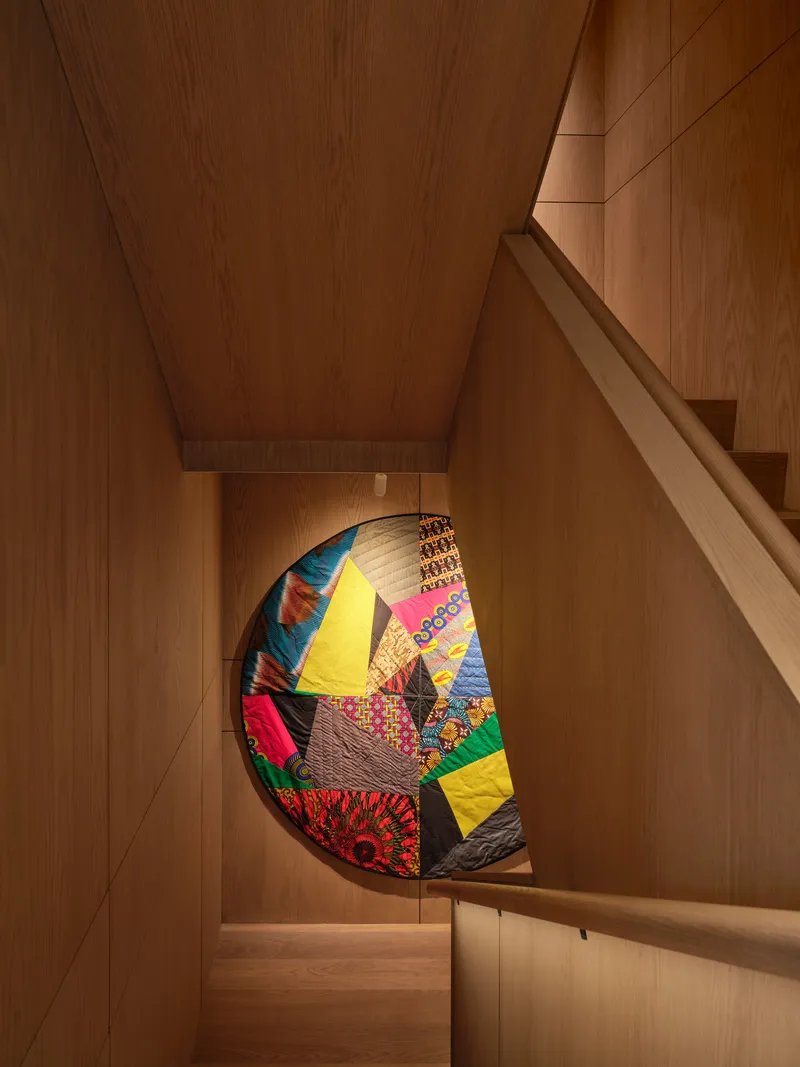 Wood-paneled staircase with patchwork quilt displayed in a recessed niche beneath the landing