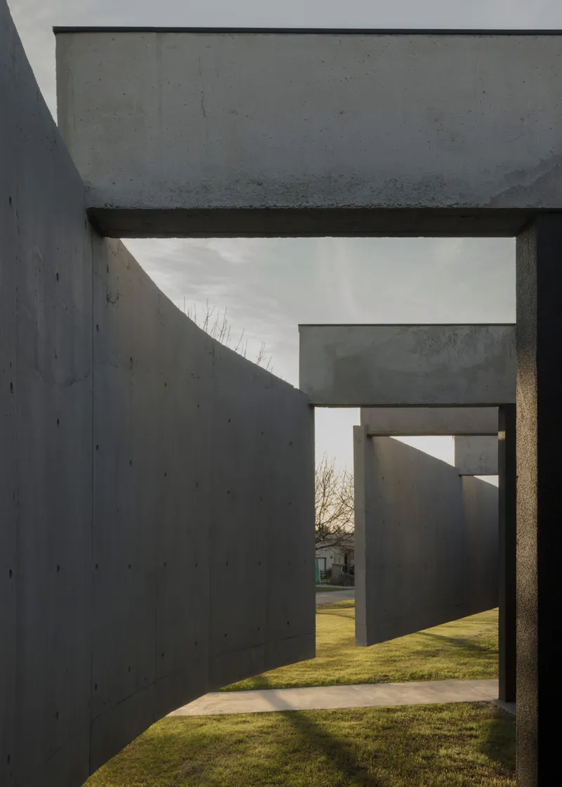 Passageway between concrete walls creating layered frames looking toward lawn and bare trees at dusk