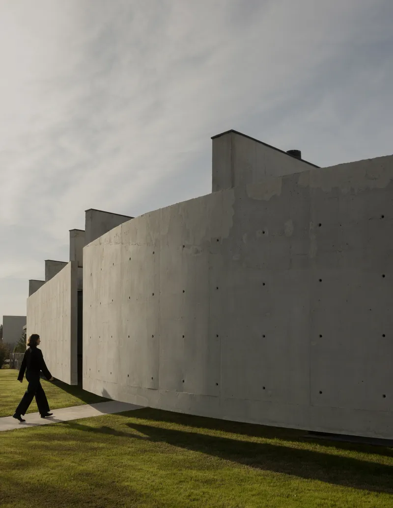 Stepped concrete facade with visible formwork ties as a figure walks along the pathway