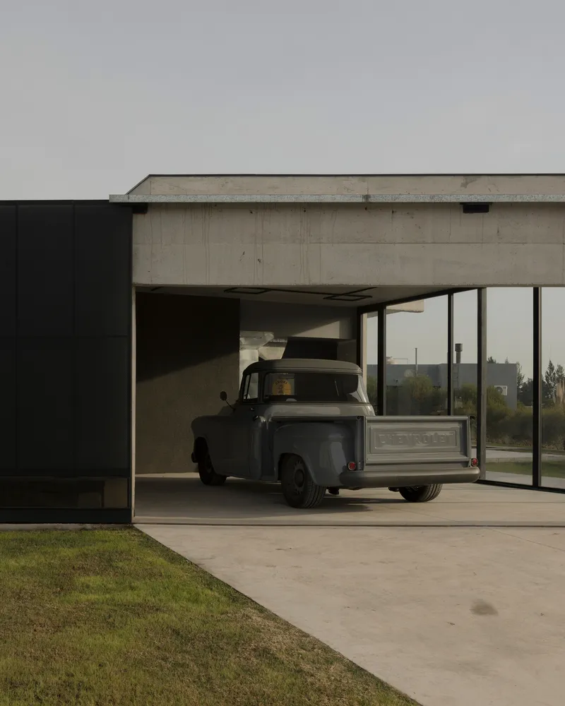 Carport with cantilevered concrete roof sheltering a vintage pickup truck at dusk