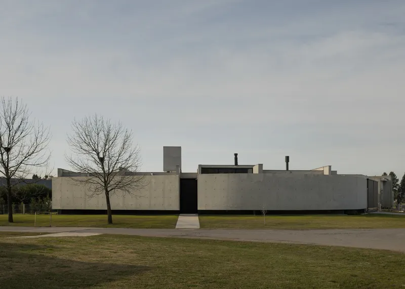 Long horizontal concrete facade with central entry flanked by bare trees on a lawn