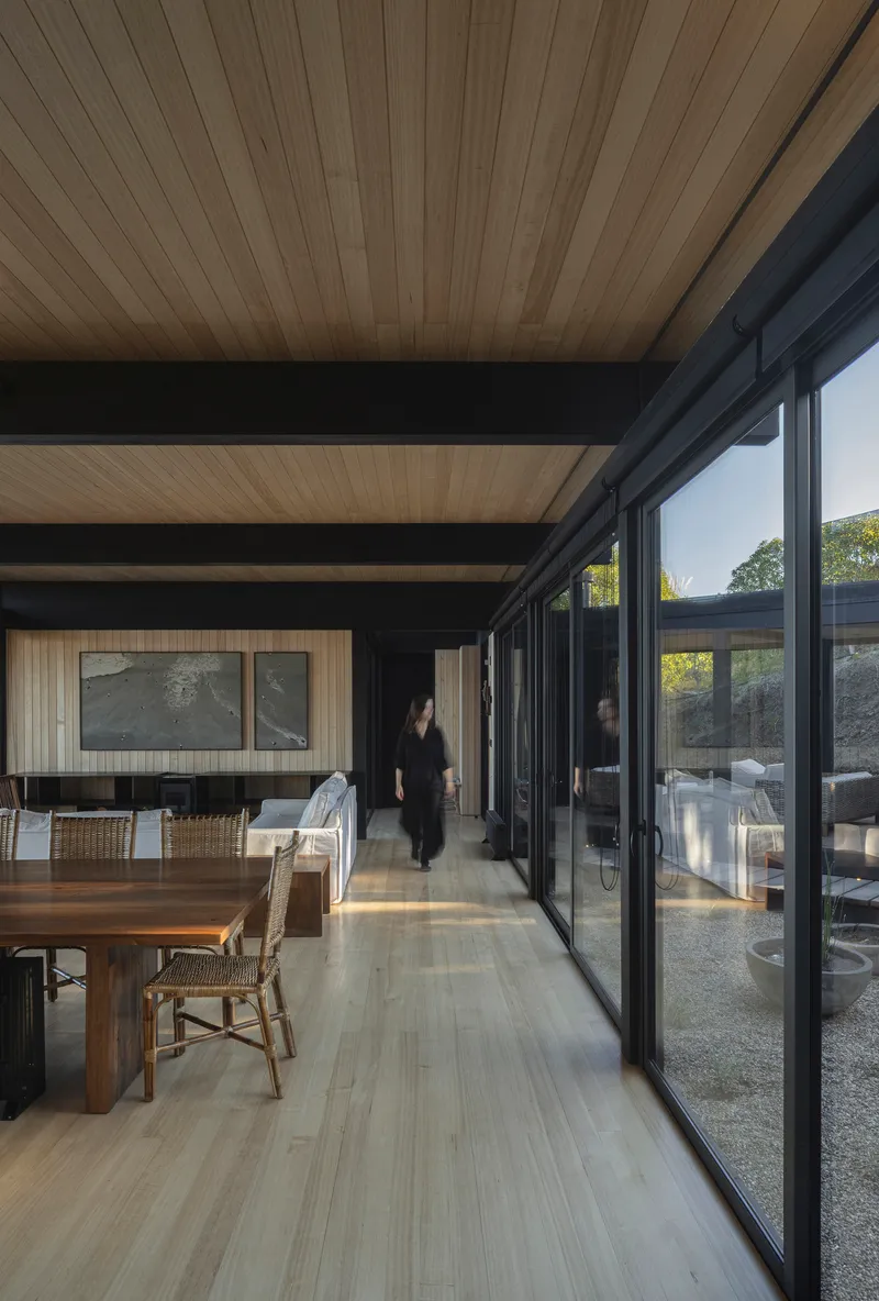 Interior corridor with timber ceiling, steel beams and sliding glass doors opening to gravel courtyard