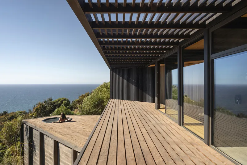 Timber deck with slatted pergola and corrugated wall panel overlooking ocean and native vegetation