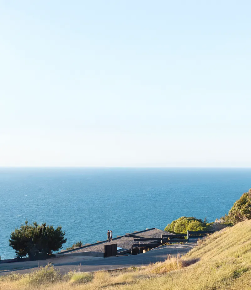 Distant view of the low-slung roof on coastal slope with two figures standing near the entrance