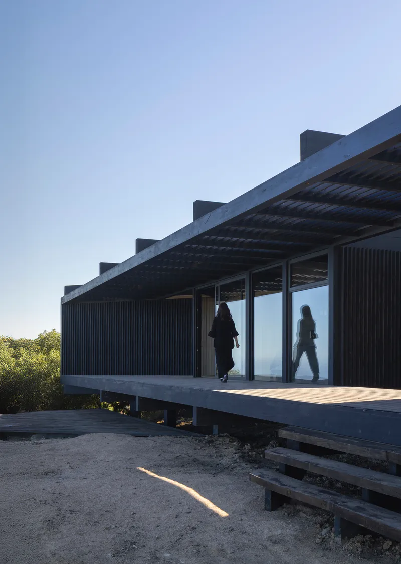 Elevated timber deck with corrugated metal cladding and residents passing through glass doors at dusk