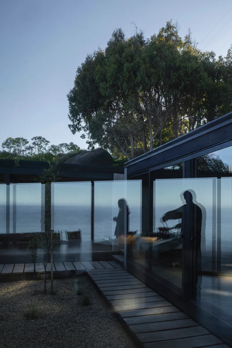 Frosted glass panels glowing at twilight with figures silhouetted against the ocean view