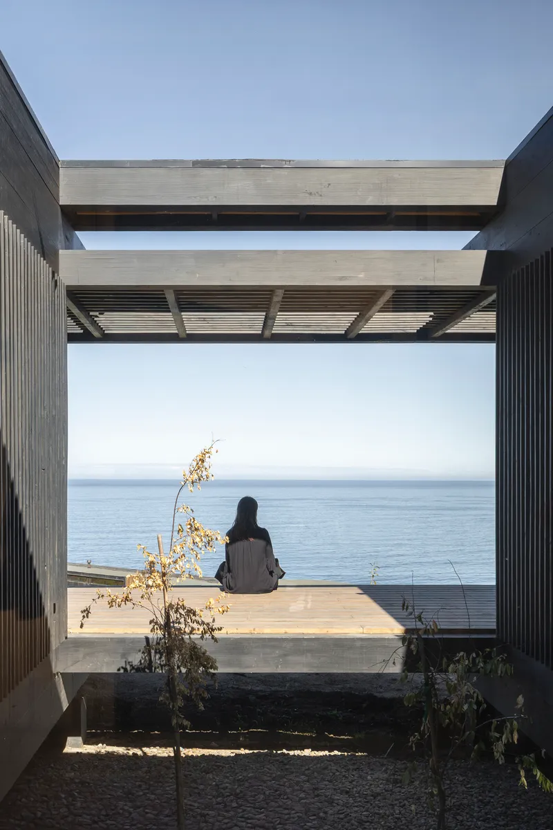 Concrete beams framing an ocean vista with a seated figure on the timber deck