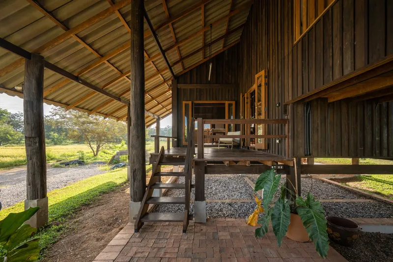 Covered ground level with wooden stair leading to elevated living space and gravel courtyard
