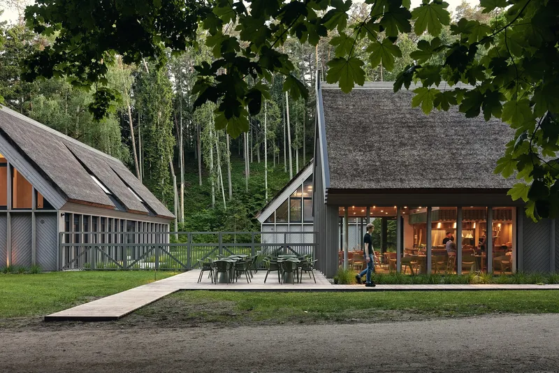 Evening view of thatched-roof pavilions with outdoor seating terrace and a person walking across the lawn