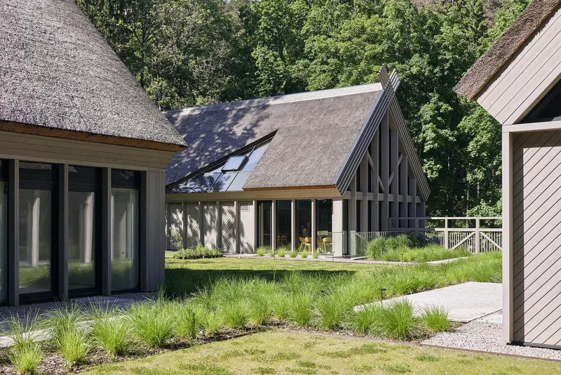 Courtyard view between thatched roof volumes with glazed facades and grassy meadow planting