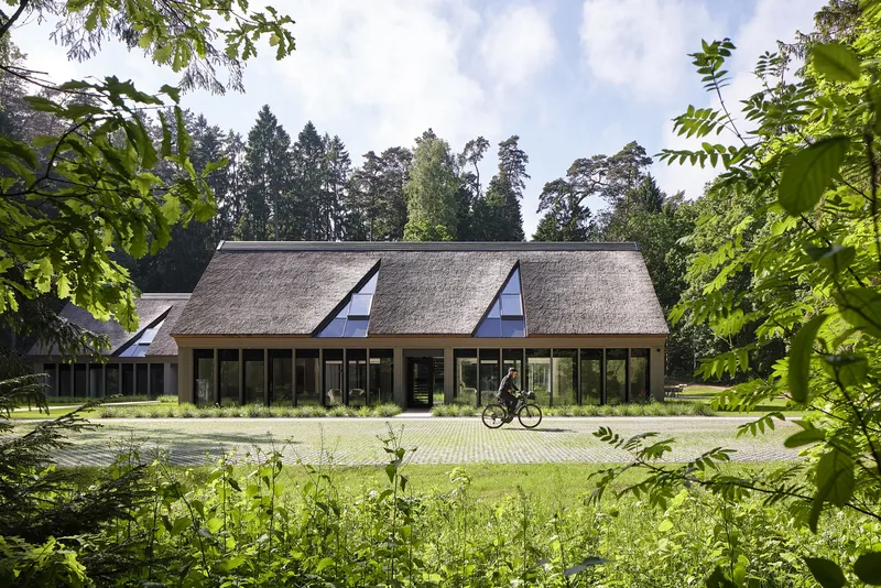 Thatched roof facade with triangular dormer windows and full-height glazing as a cyclist passes