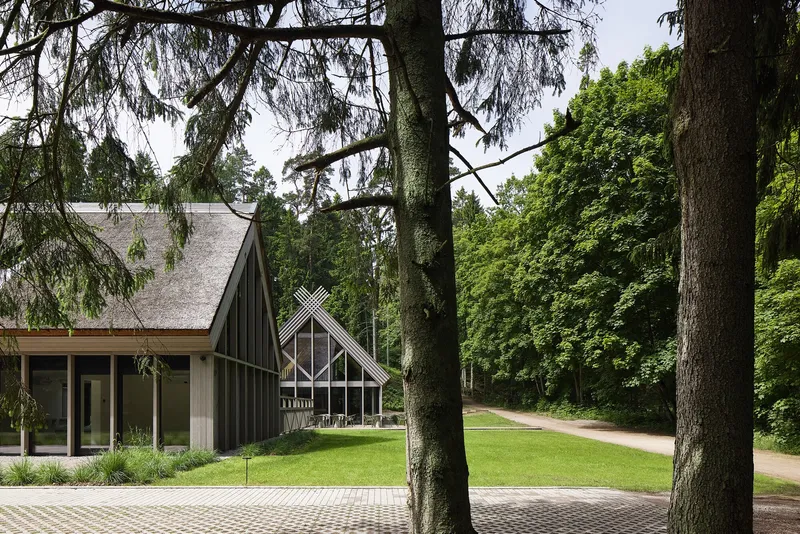 Entrance facade with vertical wood cladding and triangular glazed gable seen through tall trees
