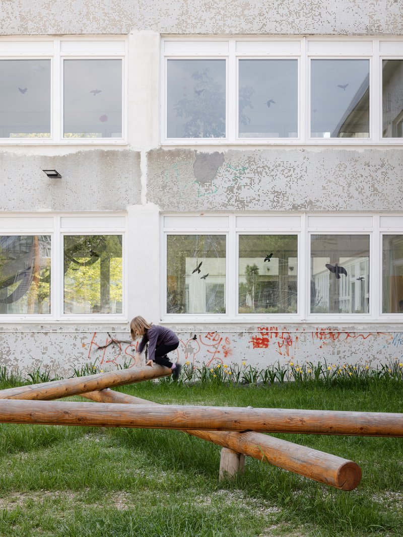 Timber balance beams on grass beside a concrete facade with windows and child-made paper decorations
