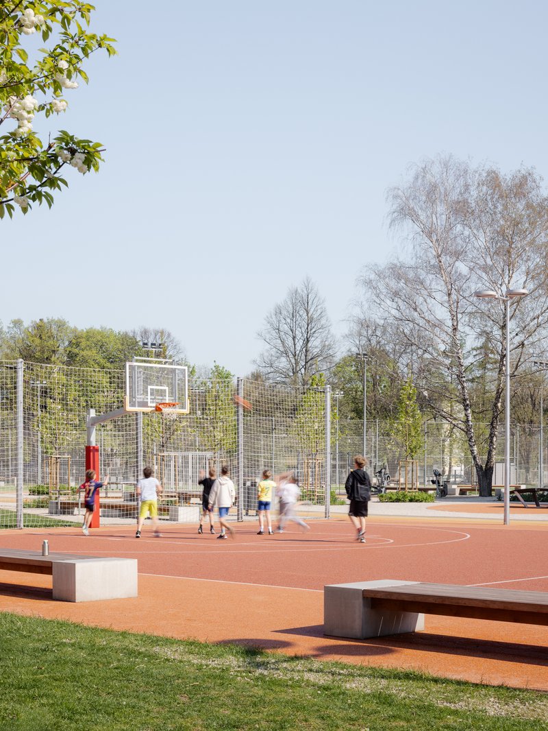 Basketball court with mesh fencing and students playing beneath bare trees