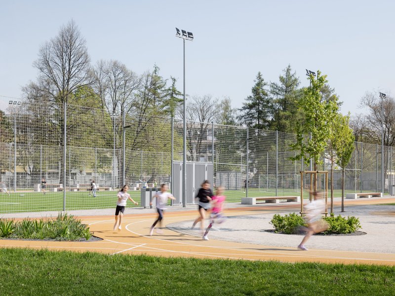 Running track with children in motion and tall wire mesh fencing backed by spring foliage