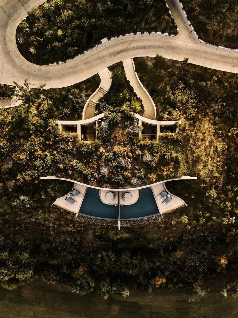 Drone view of crescent-shaped pool terrace flanked by two pavilions and curved winding paths