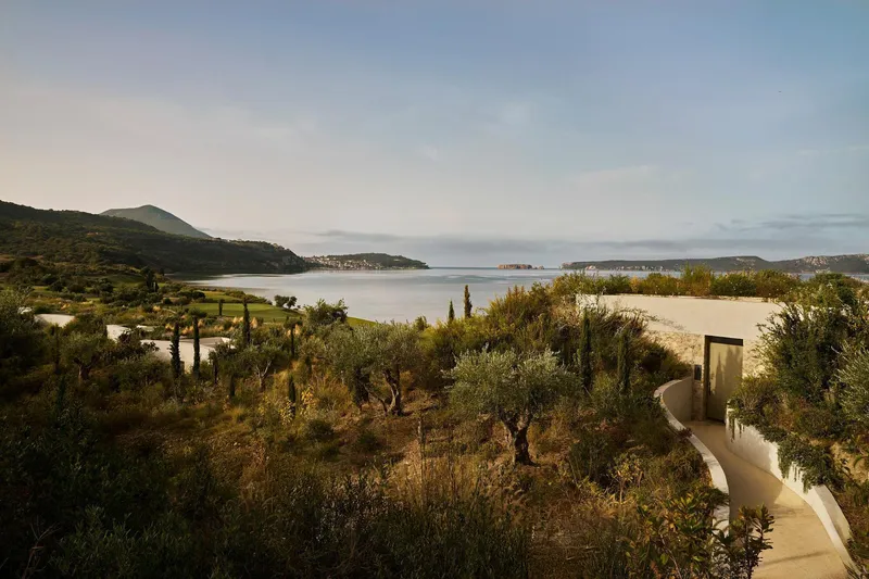 Curved roofline nestled among olive trees and cypress with coastal hills in the distance