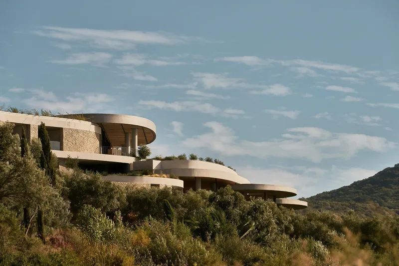 Layered circular terraces stepping down a hillside planted with olive trees and native desert vegetation