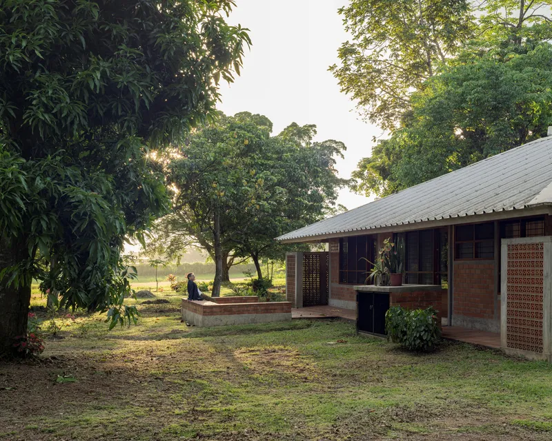 Covered veranda with corrugated metal roof and lattice screens opening onto a lawn with large trees