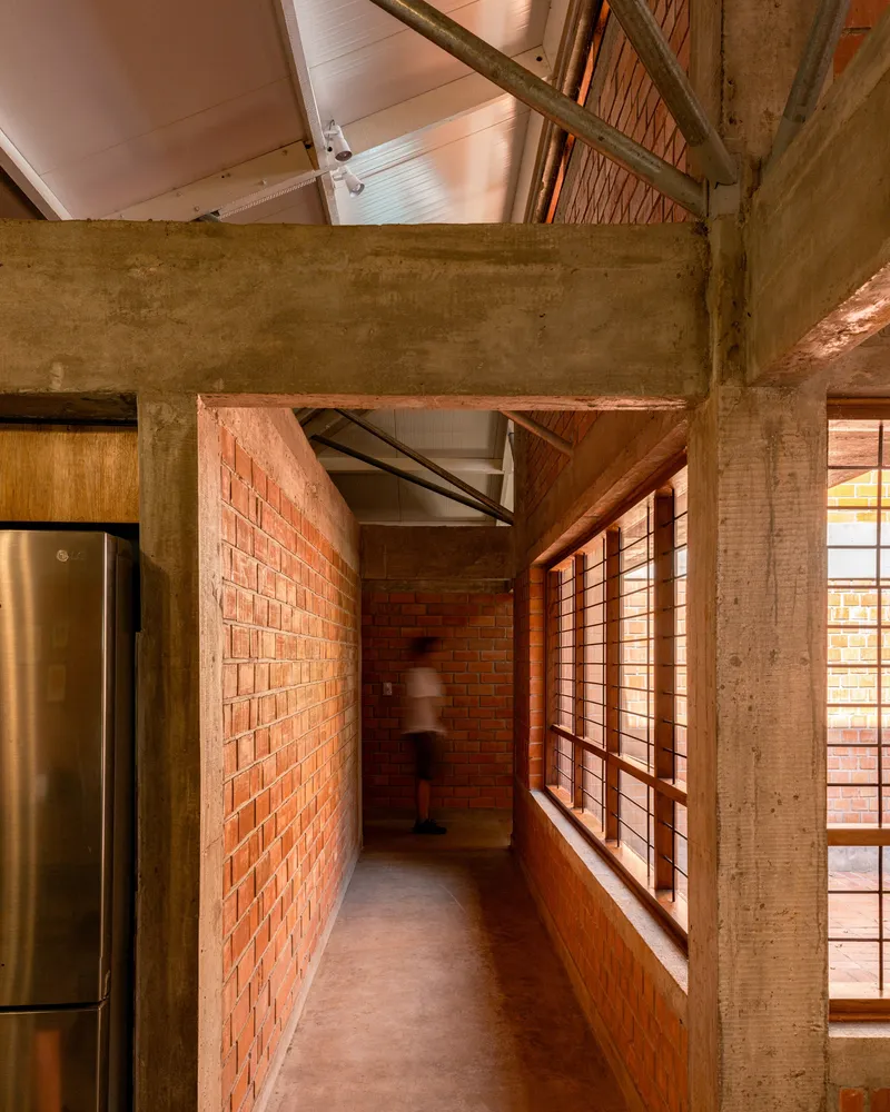 Corridor with exposed brick wall and concrete beam framing a figure in motion beneath the roof structure