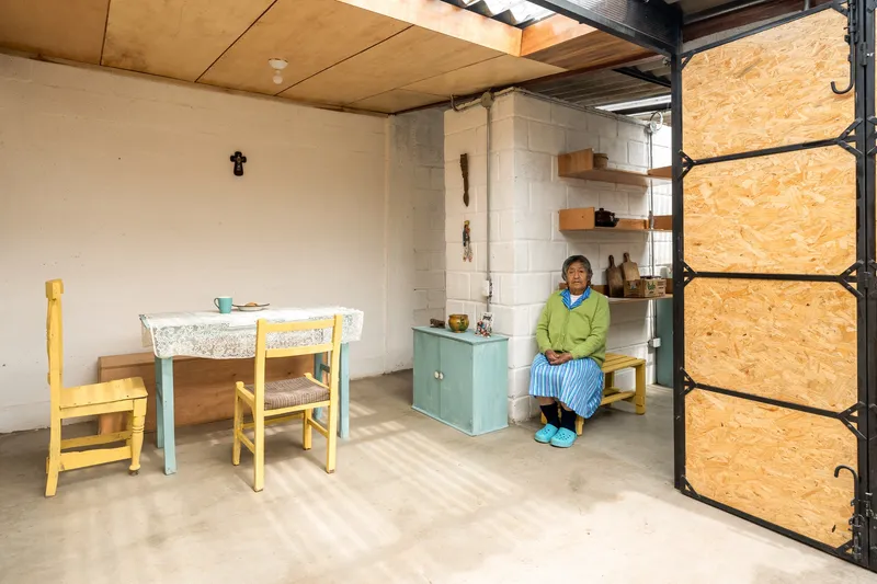Dining area with exposed corrugated metal roofing and resident seated beside open OSB door