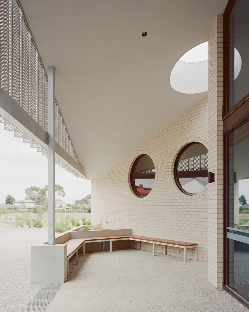 Covered courtyard with timber bench seating and circular openings in the brick wall above