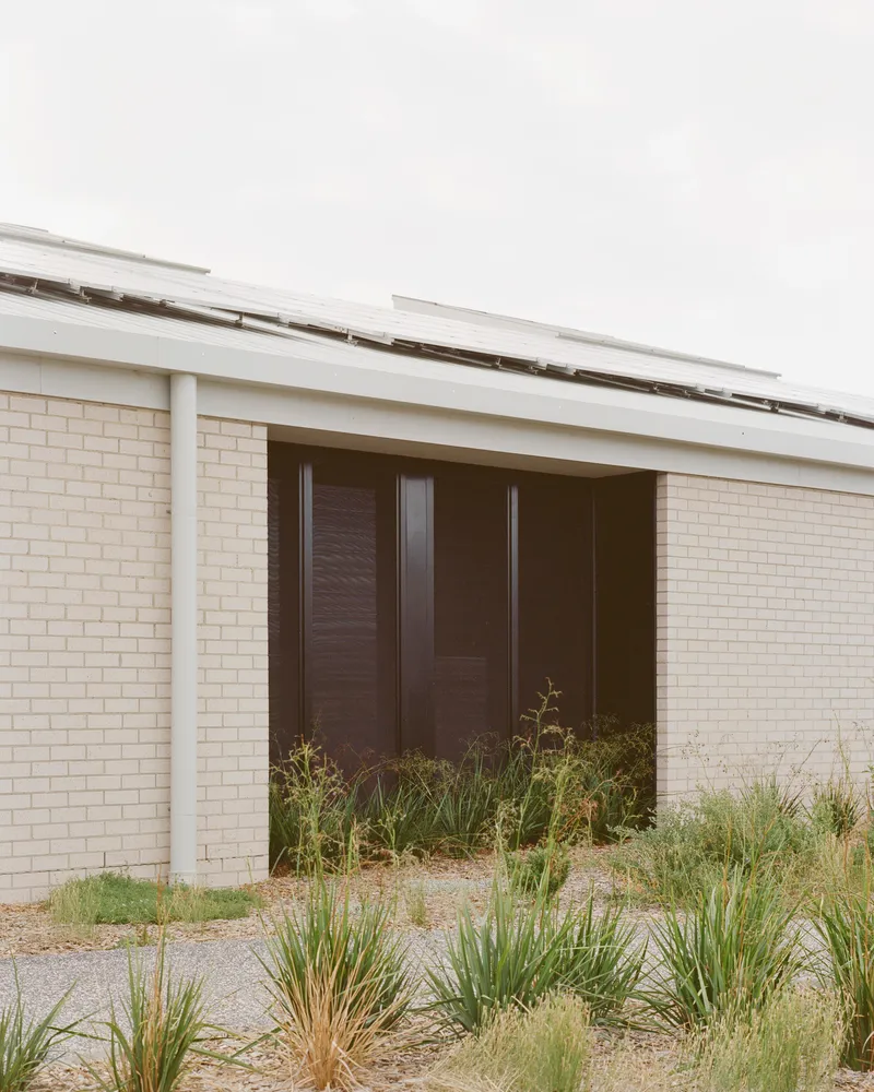 Recessed entry with dark timber doors set within pale brick walls and sheltered by a sloped metal roof