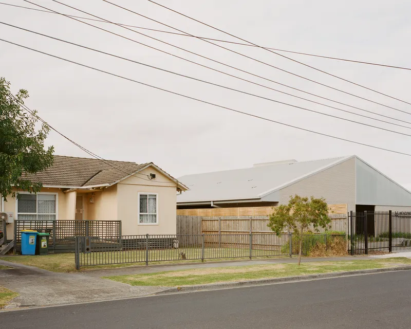 Street view of the white gabled volume beside an existing house with overhead power lines