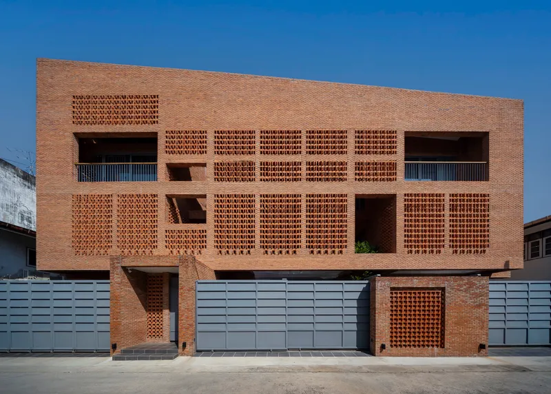 Street facade with patterned brickwork screens and grey metal gates under a clear blue sky