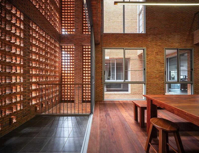Interior terrace with timber furniture alongside backlit perforated brick screen wall at dusk