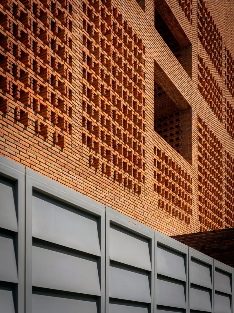 Textured brick facade with alternating solid and perforated patterns above white metal paneling in afternoon light