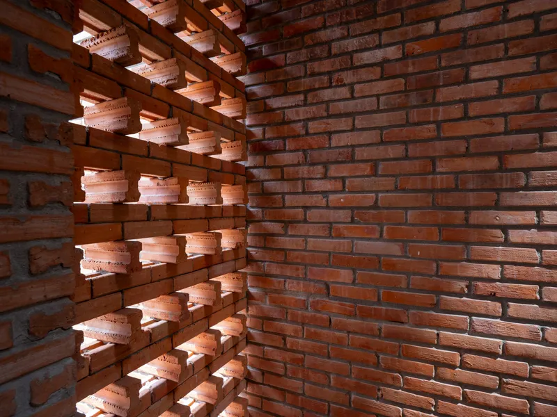 Corner detail where perforated brick screen meets solid brick wall with exposed timber joists above