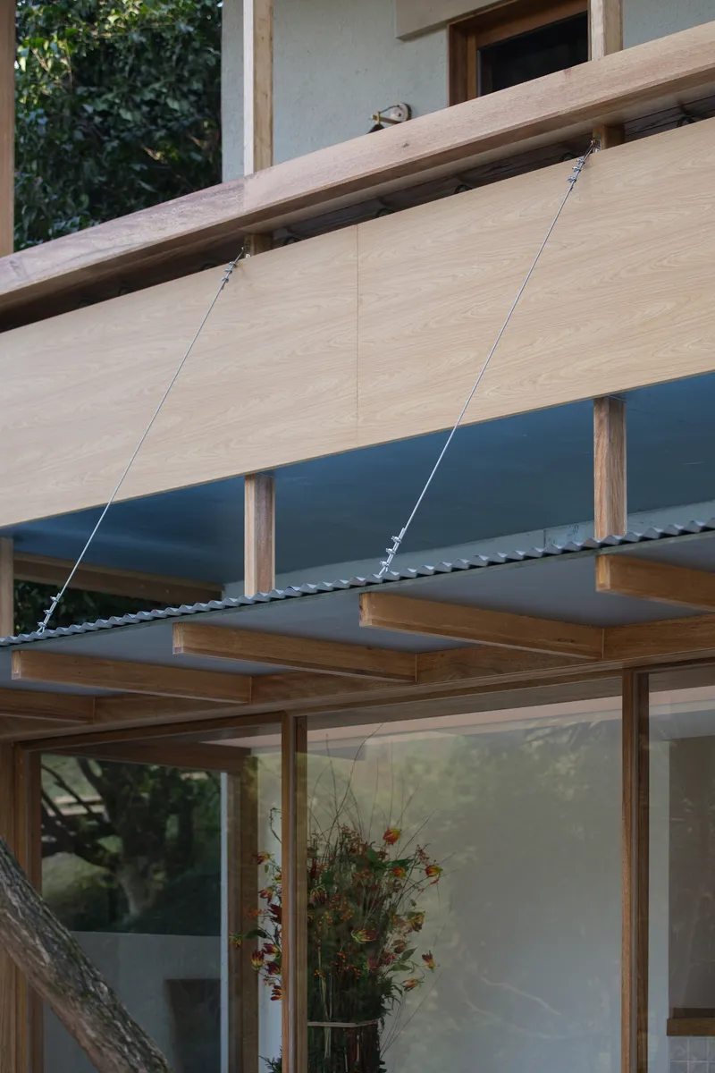 Timber overhang with cable suspension system above glazed opening and timber frame below