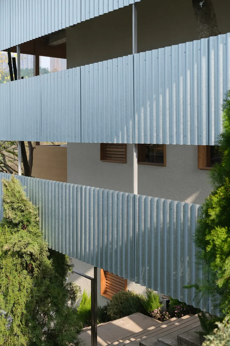 Stacked facade with corrugated metal panels and horizontal strip windows surrounded by trees