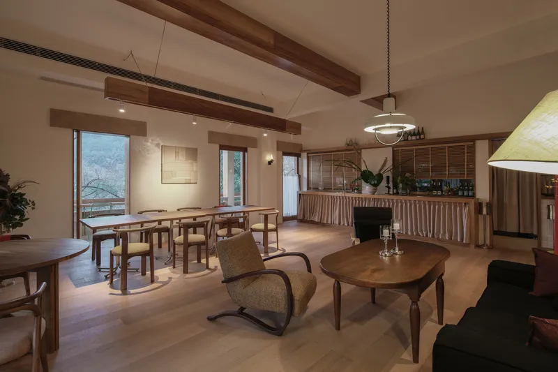 Open dining and lounge space with exposed timber beams and a bar counter under evening lighting
