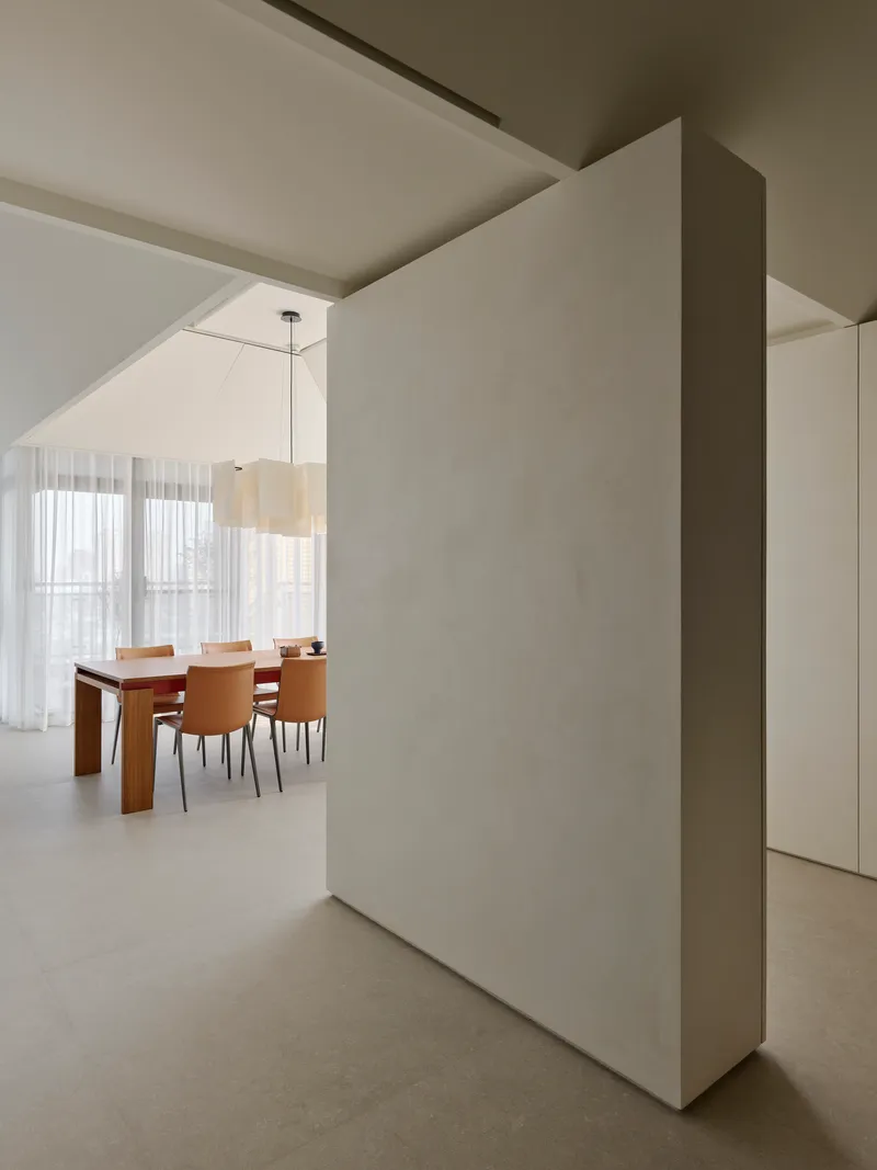 Freestanding partition wall separating spaces with dining area visible through sheer curtained windows beyond