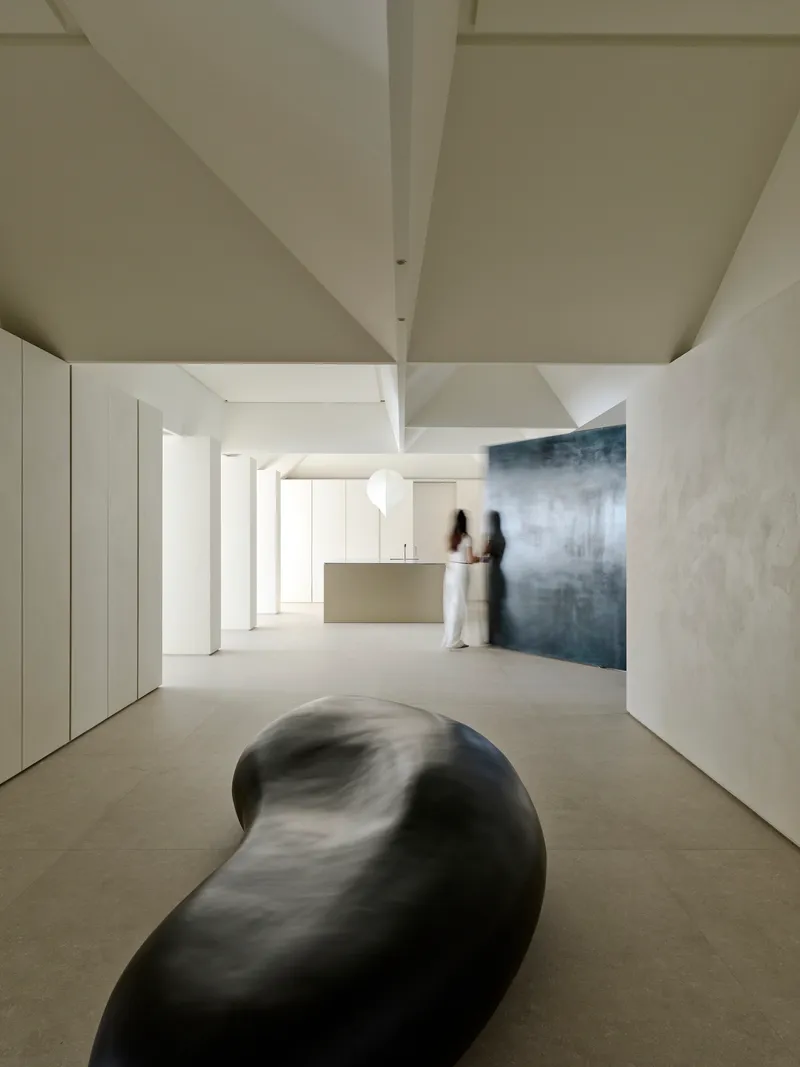 Open living space with sculptural black form on floor and two figures near kitchen island