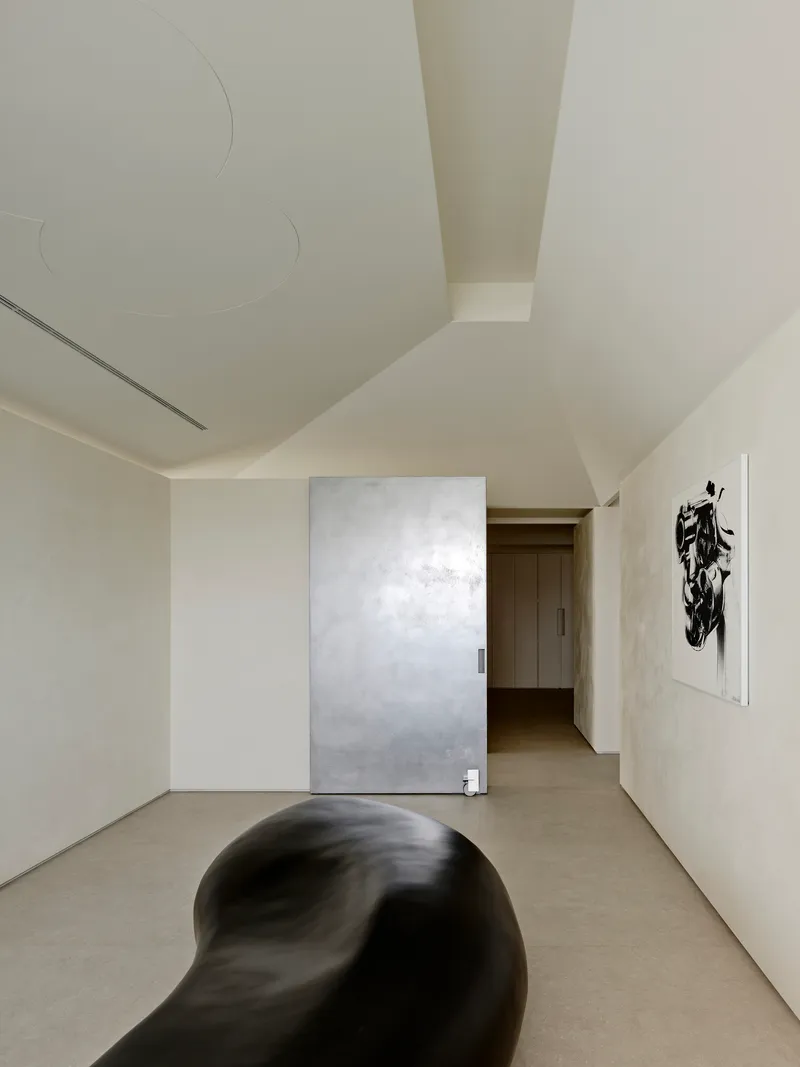 Hallway with sliding metallic door panel and artwork beside organic black sculpture on concrete floor