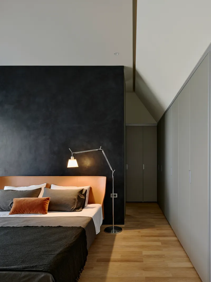 Bedroom with articulated task lamp beside bed against charcoal accent wall and timber flooring