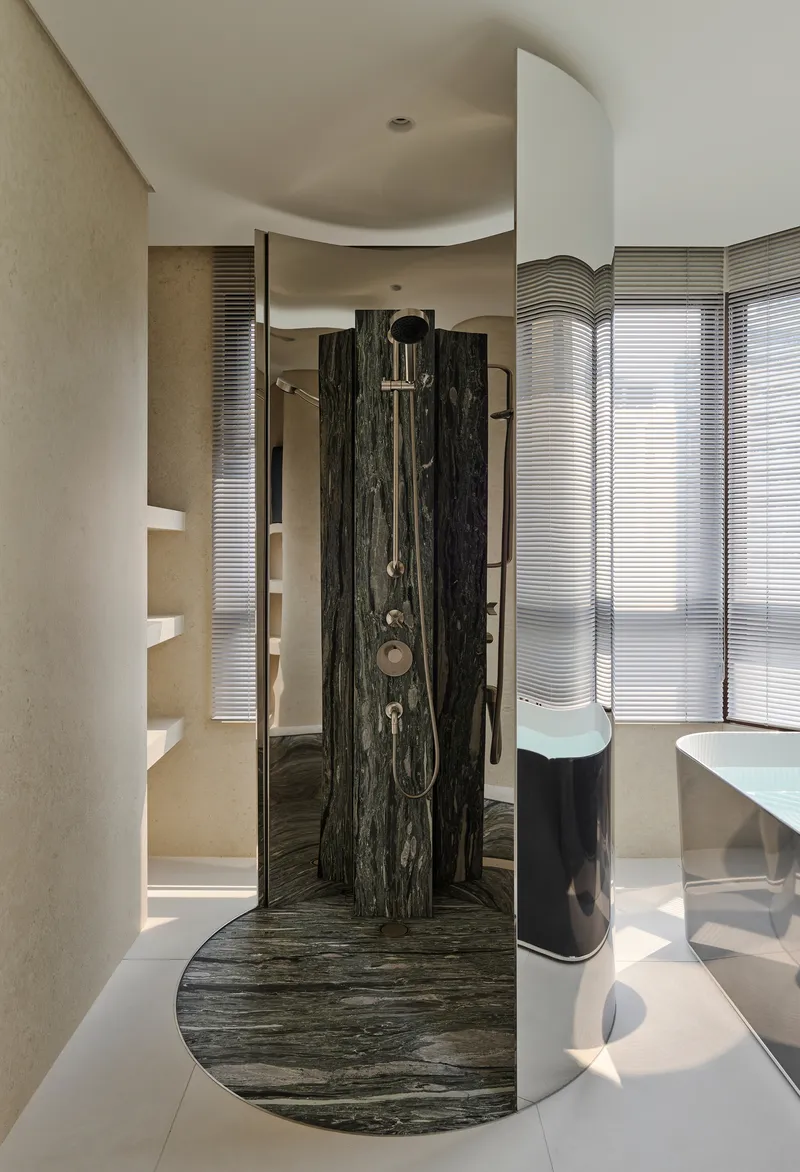 Freestanding shower with veined black marble surround and curved base beneath fluted glass windows