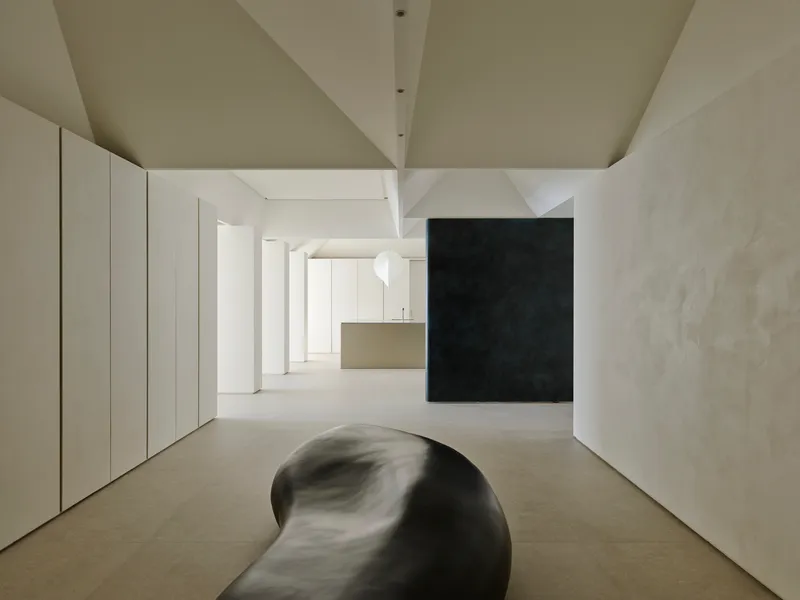Open interior with curved black sculpture on the floor beneath angular white ceiling planes and textured columns