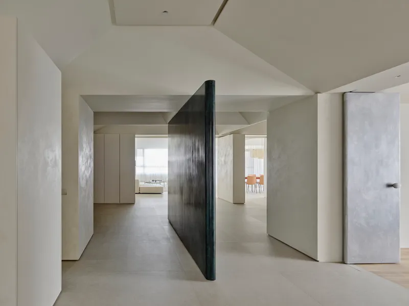 Pivoting dark metal partition between pale plaster walls with view through to daylit rooms beyond