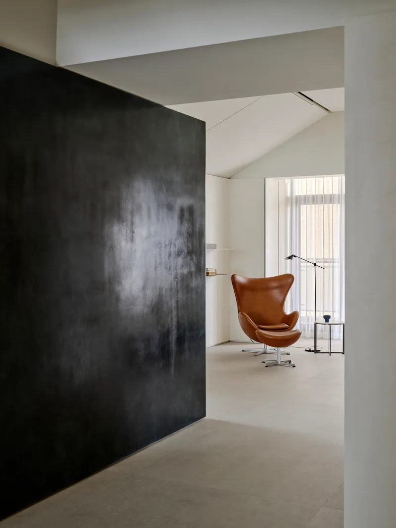 Dark textured wall panel framing a tan leather chair beside a floor lamp and window