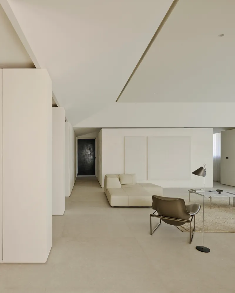 Living area with recessed lighting channel in the ceiling and dark panel visible in hallway distance