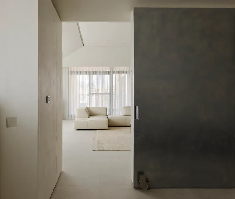 Narrow corridor framed by dark sliding panel opening to sitting area with sheer curtains
