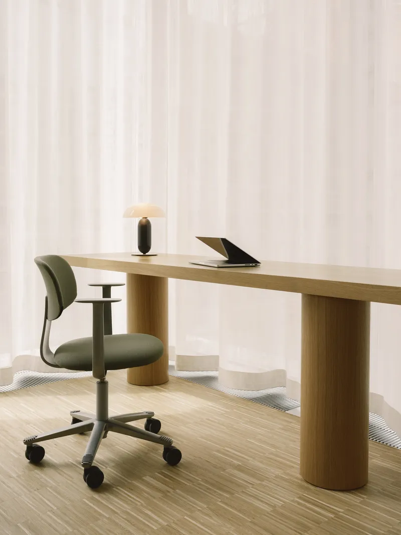 Workspace with cylindrical timber desk legs and upholstered task chair on casters beside white sheer drapery