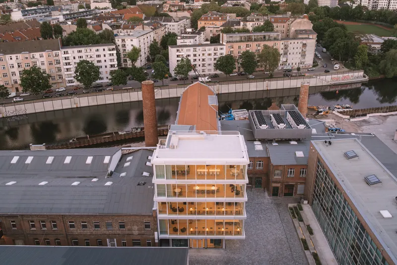 Aerial view of the white glass volume rising among industrial rooftops and a river beyond