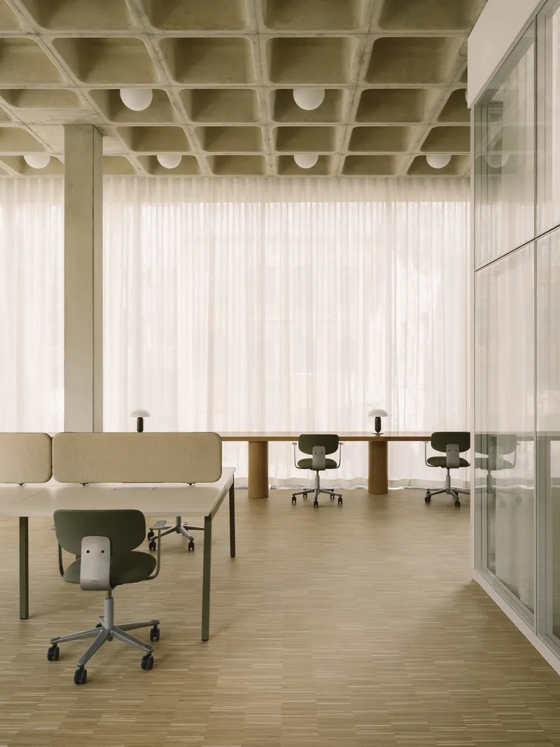 Open workspace with waffle concrete ceiling, globe pendant lights, and workstations near floor-to-ceiling curtains