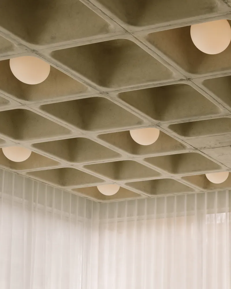 Upward view of waffle concrete ceiling with recessed globe fixtures behind translucent curtain panels