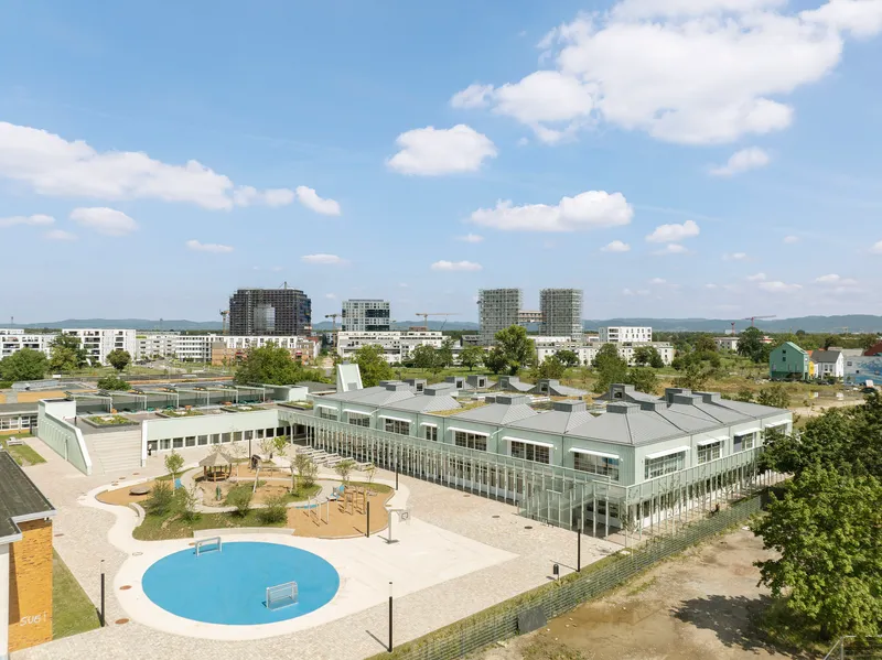 Aerial view of the pale green corrugated roofscape with circular blue pool in the foreground plaza